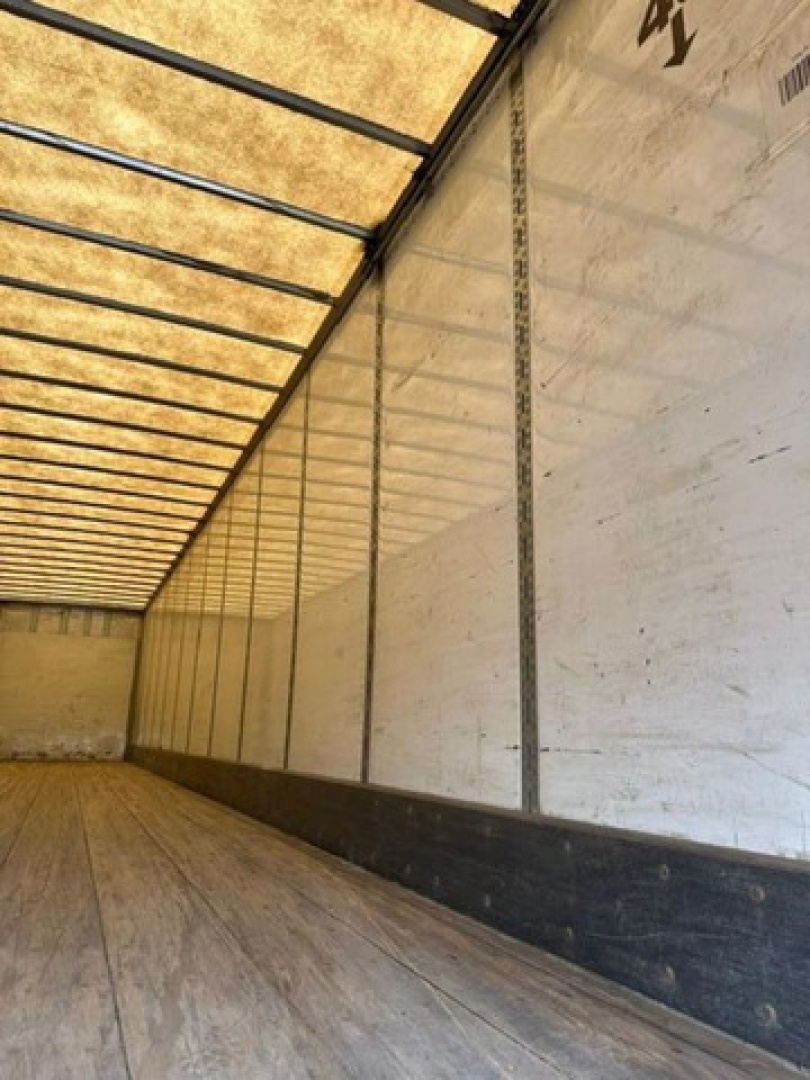 Trailer interior showing long empty cargo area with wooden floor and white side walls and ribbed ceiling panels.