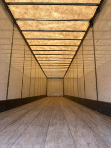 Interior of a 2016 Wabash van trailer showing wooden floor, side walls, and overhead framing with dim lighting at the far end.