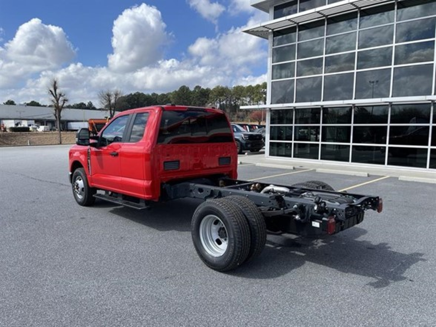 Ford F-350 chassis cab showing rear chassis and single rear wheel, red cab, dealership lot in background.