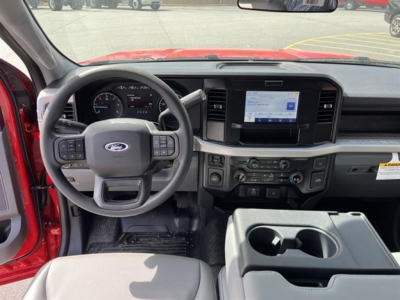 Ford interior cabin showing steering wheel with controls, large center touchscreen, and dual cup holders in front row; dashboard and gauges visible.