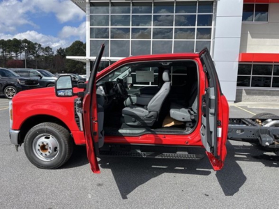 Vehicle interior image showing a red 2026 Ford F350 Sd cab and chassis with doors open, showing driver seat, steering wheel, and dashboard. No visible text on components.