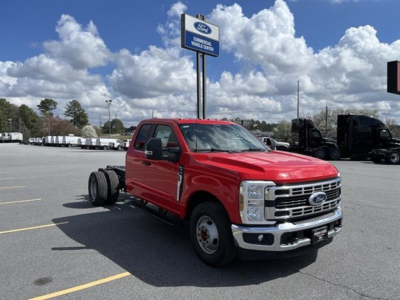 Front-left view of a red 2026 Ford F-350 SD cab and chassis truck in a dealership lot, chrome grille, dual rear wheel peeking, blue sky with clouds.