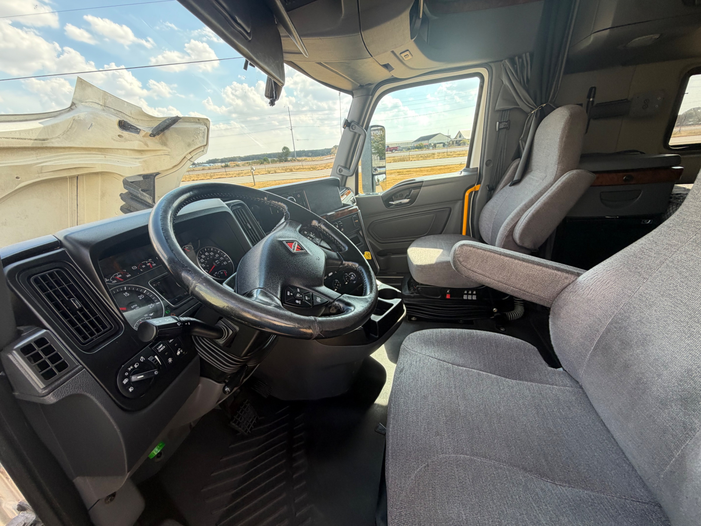 Truck cab interior of a 2021 International LT625 shows steering wheel, dashboard, and driver seat from the passenger side with gray fabric seats.