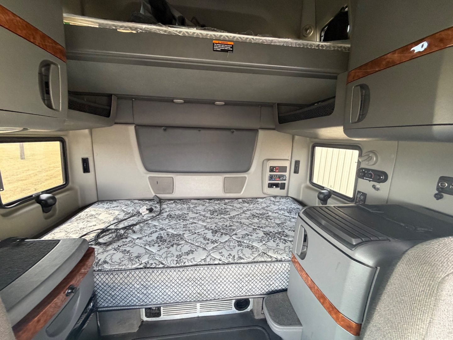 Interior cabin of 2021 International LT625 sleeper showing rear bed area with storage cabinets and overhead bunk area.