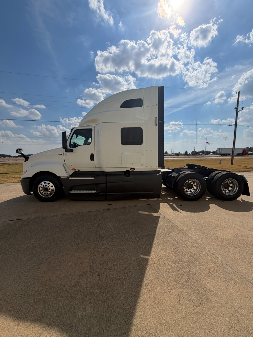 International LT625 truck cab and chassis side profile showing sleeper cab and triple rear axles in a parking lot.