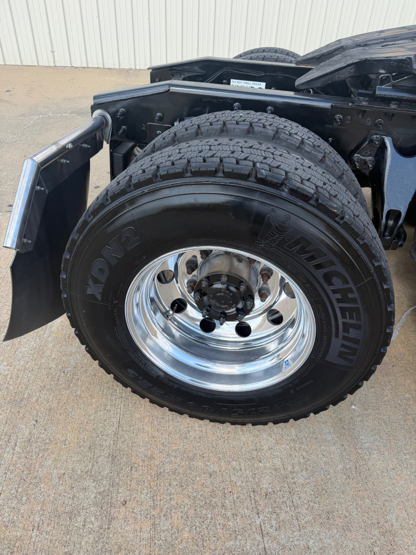 Truck wheel and fender showing a Michelin XDN2 tire mounted on a polished steel wheel; part of the drivetrain and suspension visible.