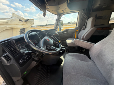 Truck cab interior of a 2021 International LT625 shows steering wheel, dashboard, and driver seat from the passenger side with gray fabric seats.