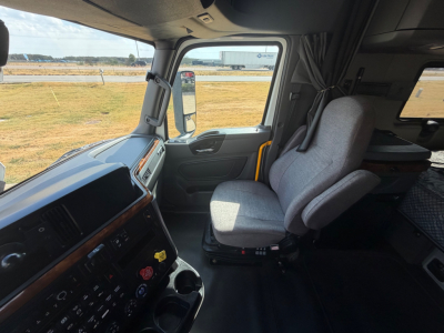 Truck cabin interior showing steering wheel, dashboard, and a gray driver seat with large side mirror visible through the window.