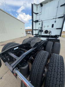 Tractor with drivetrain exposed, hitch and dual rear axles on a semi truck chassis, cab at rear, various hoses and components visible.