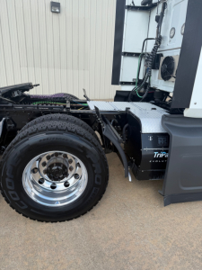 Truck cab and front wheel area of a 2021 International LT625 showing front wheel, fuel lines, and side step with TriP... branding visible.