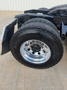Truck wheel and fender showing a Michelin XDN2 tire mounted on a polished steel wheel; part of the drivetrain and suspension visible.