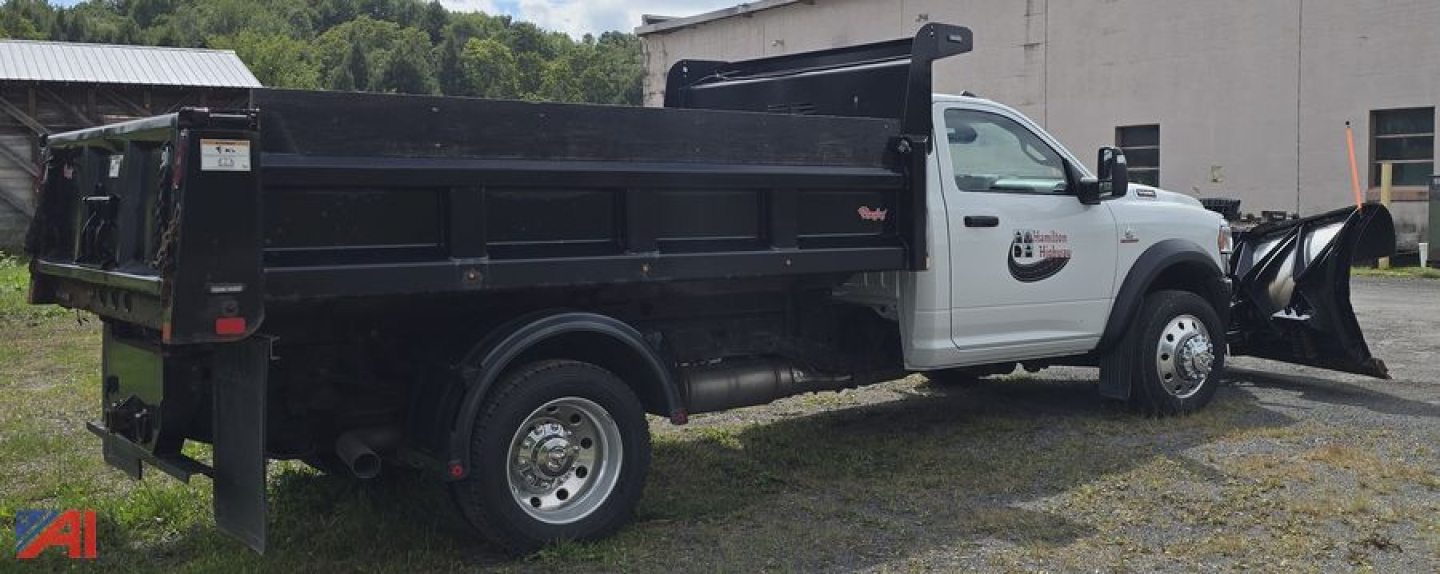 Ram 5500 dump truck with plow attachment and black dump bed, side view in a lot