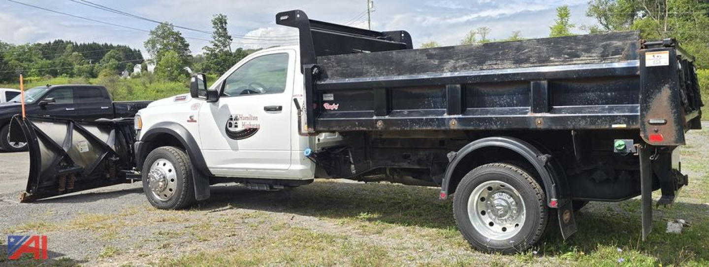 Truck chassis showing 2023 Ram 5500 single cab dump bed with plow attachment on front, side view, black dump bed, white cab, logo on door, utility lights