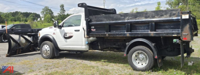 Truck chassis showing 2023 Ram 5500 single cab dump bed with plow attachment on front, side view, black dump bed, white cab, logo on door, utility lights