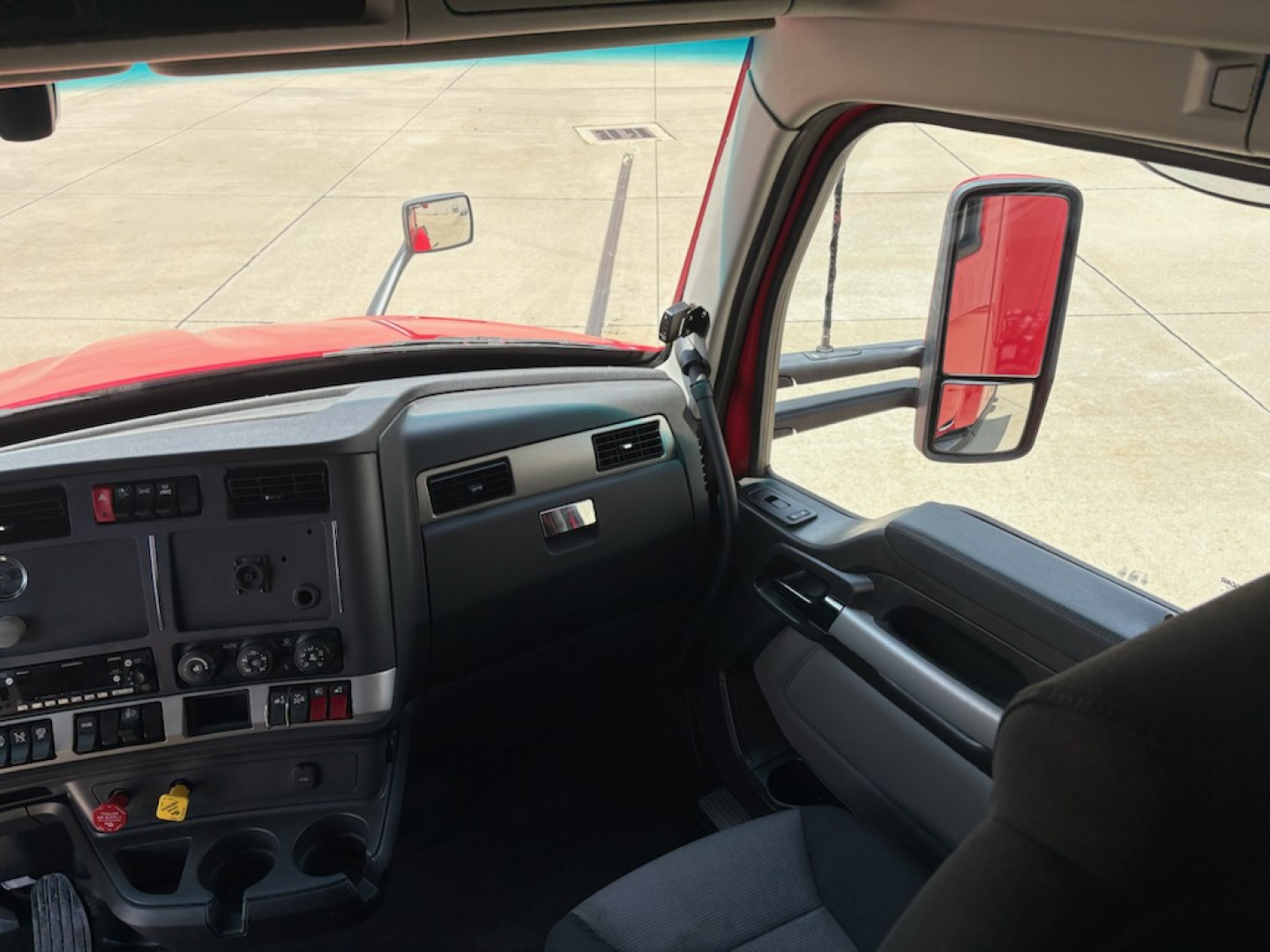 Truck cab interior of a 2024 Kenworth T680 showing dashboard controls, steering wheel, and side mirror; no visible fluid labels or equipment data.