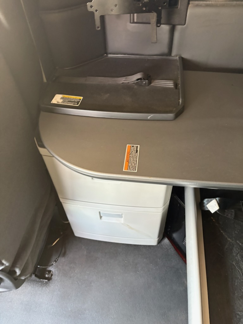 Cab interior of a Kenworth T680 sleeper showing a storage drawer, a fold-out table surface, and a small cabinet with a contoured edge.