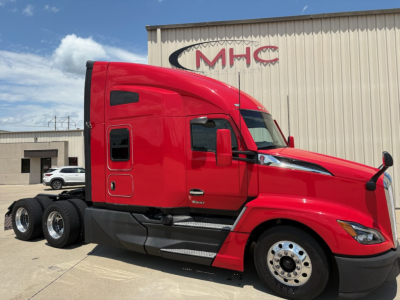 2024 Kenworth T680 truck front-left side showing red sleeper cab and front wheel, dealership building in background with MHC logo.