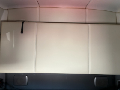 Kenworth T680 sleeper cab interior rear storage area with light-colored upholstery and a strap on a panel.