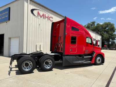 Kenworth T680 tractor in red with sleeper cab, side view showing chassis and rear axles parked outside a service building.