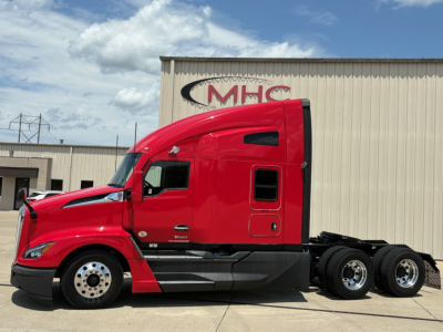 Kenworth T680 truck side view showing red cab and sleeper, three rear axles, and dealership building in background.