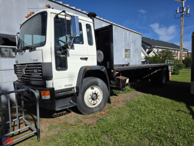 Volvo FE flatbed truck in-service showing front grille with Volvo emblem, cab door text 'FE', and flatbed behind. Visible markings include a spare tire on the side and a black bumper.