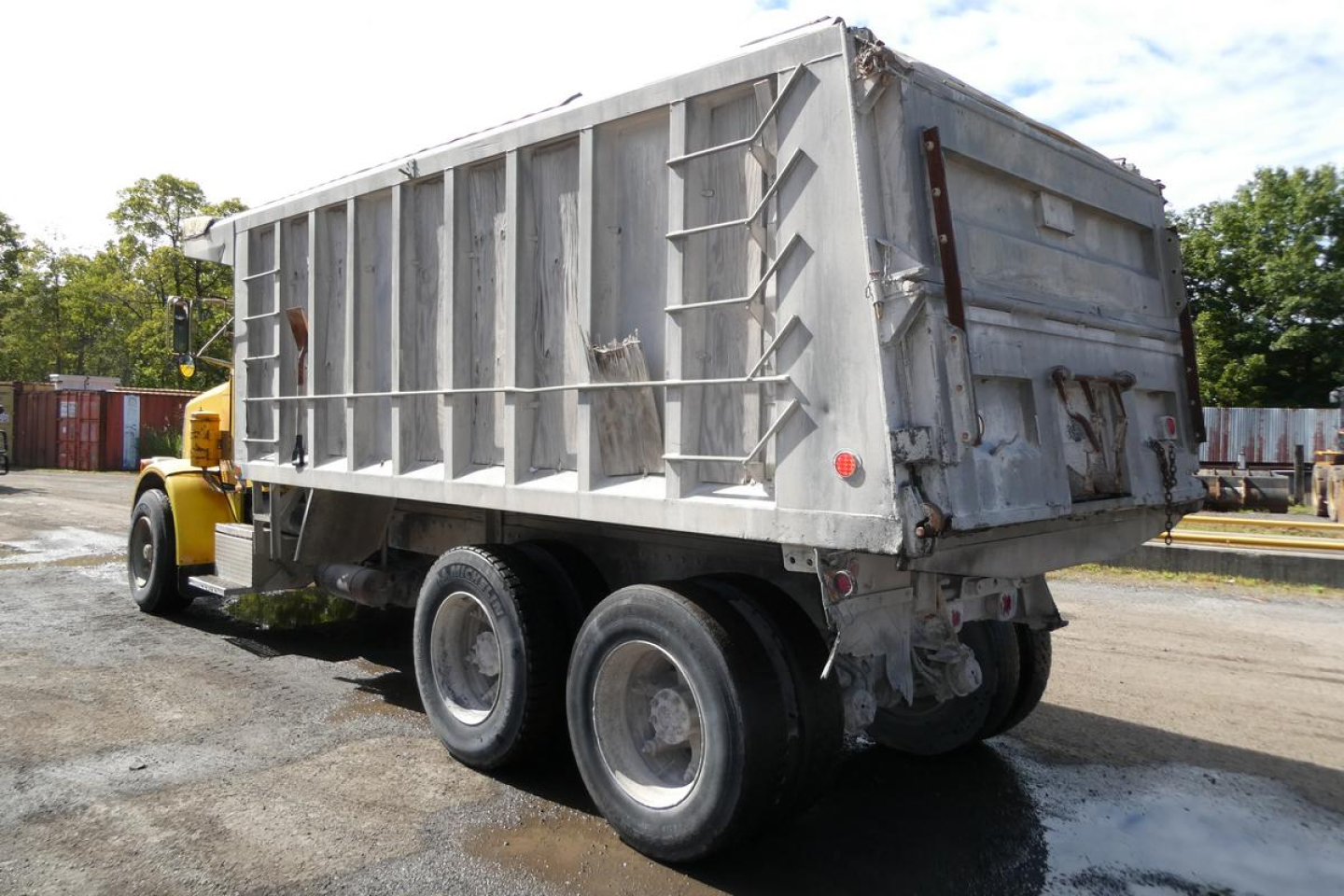 Peterbilt dump truck rear three-quarter view showing large aluminum dump bed with six-wheel tandem axle and rear tailgate.
