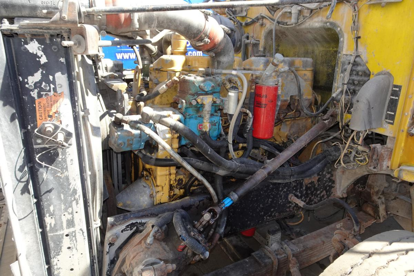 Peterbilt dump truck engine bay with visible hoses, blue engine blocks, red oil filter, and yellow cab frame in-service machinery.