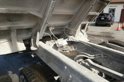 Dump truck rear frame and dump bed hinge area showing metal frame, hydraulic lines, and wheel on a Peterbilt 357.