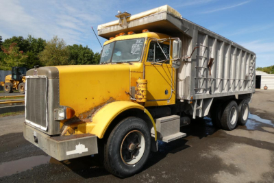 Dump truck 1987 Peterbilt 357, yellow cab with gray dump body, front view angled, VIN 1XPALB0X2HN250809 visible on windshield.