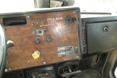 Peterbilt 357 dash panel with wooden finish showing switches and gauges; handwritten label and yellow knob visible.