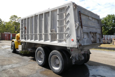 Peterbilt dump truck rear three-quarter view showing large aluminum dump bed with six-wheel tandem axle and rear tailgate.