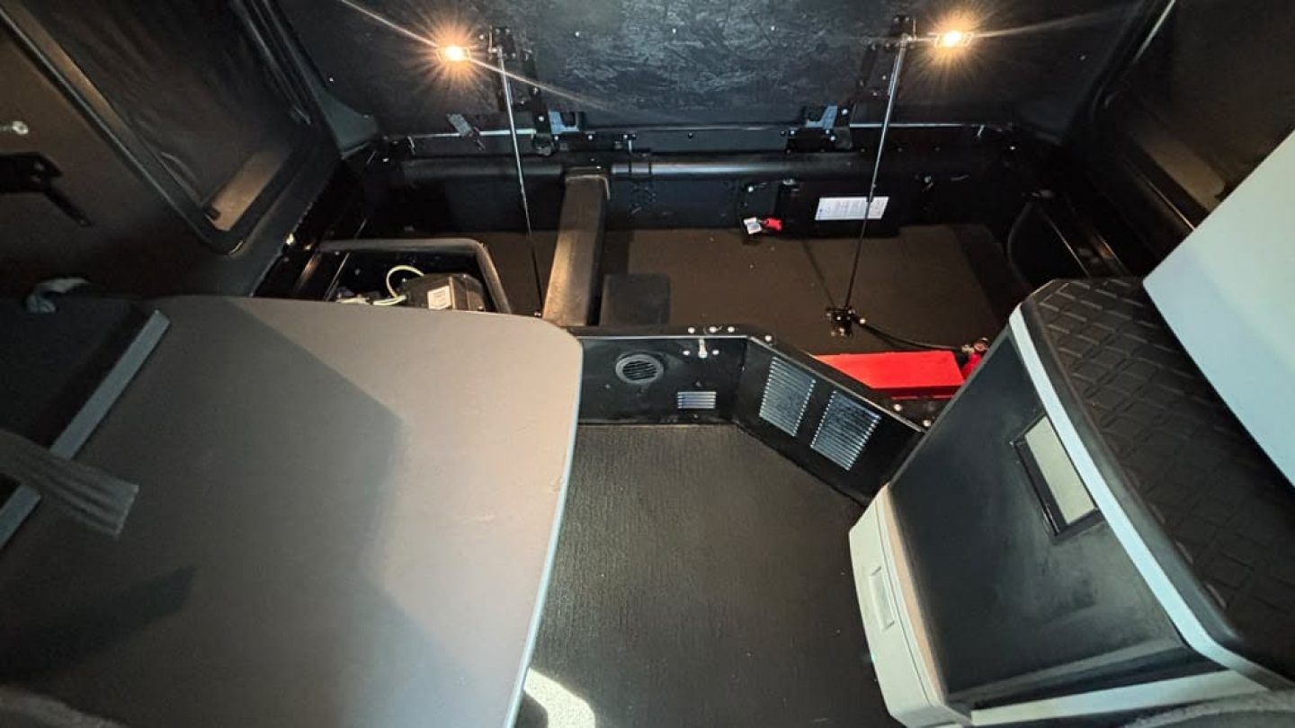 Interior view of a Kenworth T680 cab showing driver seat and dashboard area with center console and storage compartments.