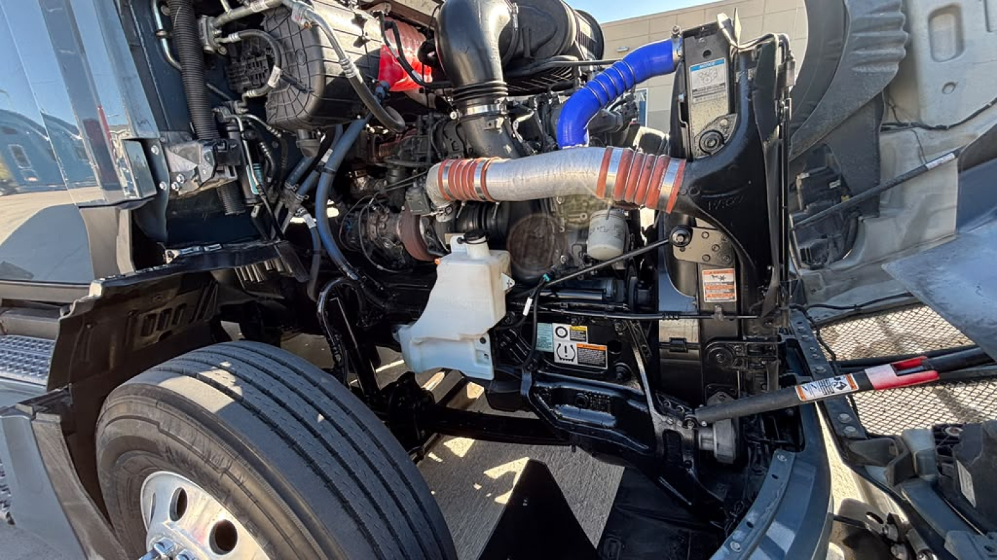 Kenworth T680 engine bay showing cooling system hoses, radiator, and intake manifold with various pipes and components visible.