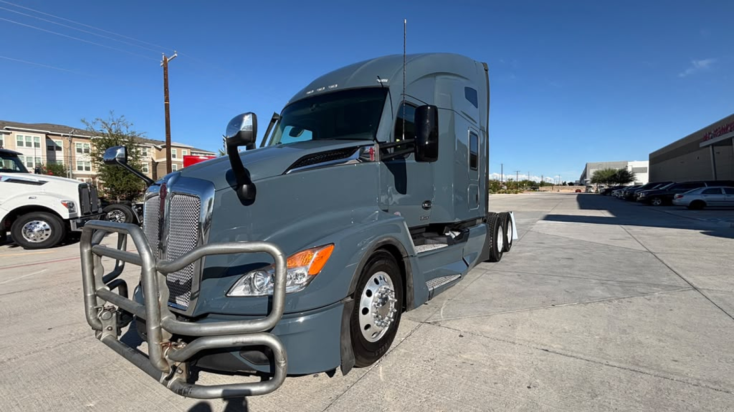 Kenworth T680 standard wheelbase sleeper cab tractor in blue-gray color with front grille guard. Side view shows large side mirrors, aerodynamic sleeper, and chrome wheels.