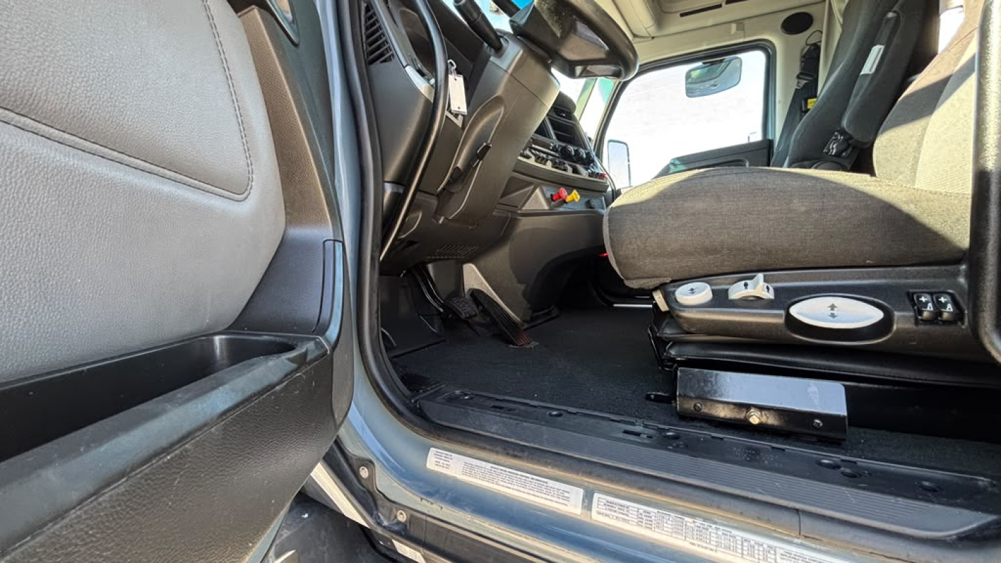 Kenworth T680 interior cab entry showing front seat and driver's area with controls and floor mat, side step and door sill visible.