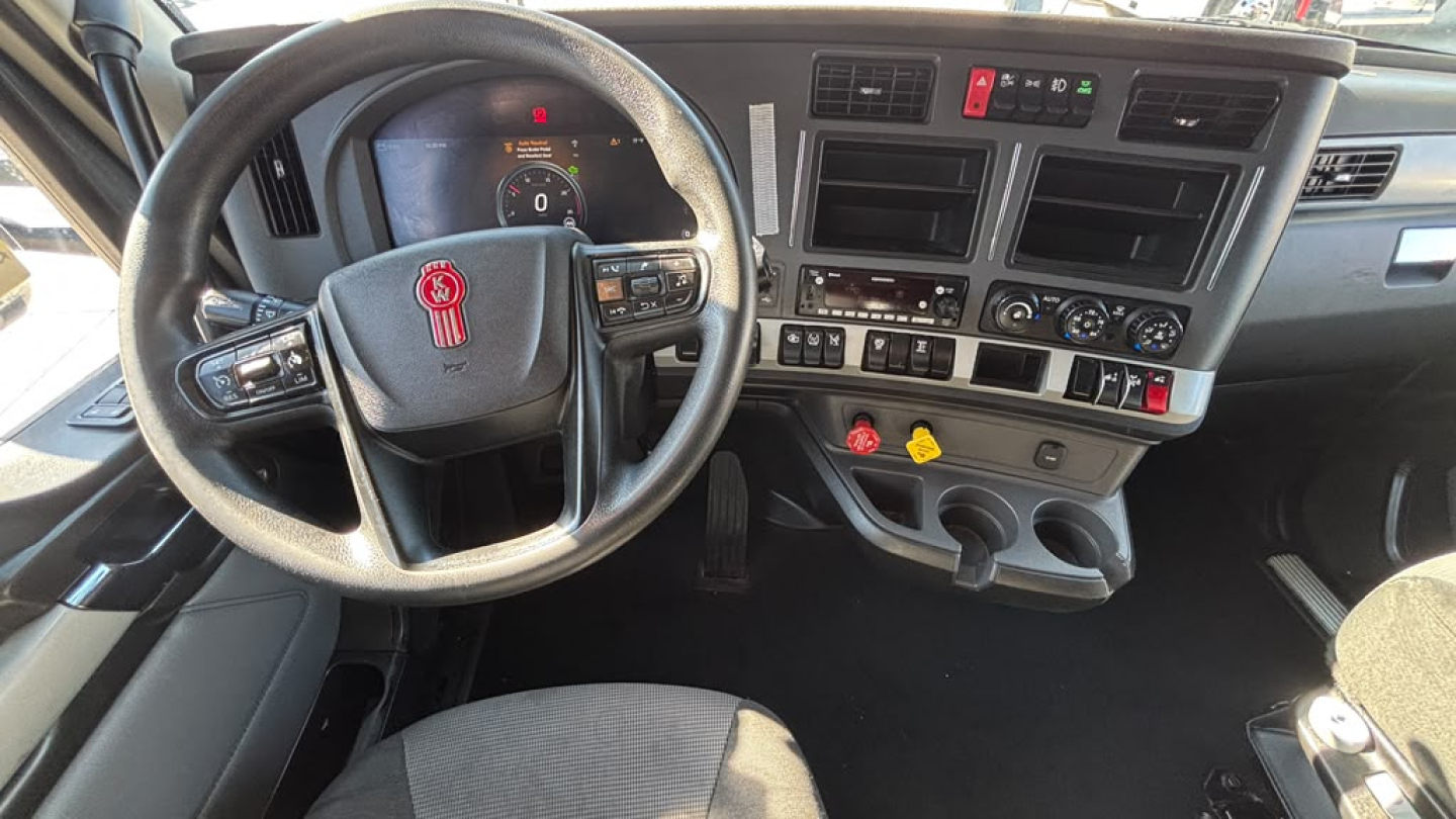 Kenworth T680 interior dashboard view with steering wheel, gauge cluster, and center console showing controls and cup holders.