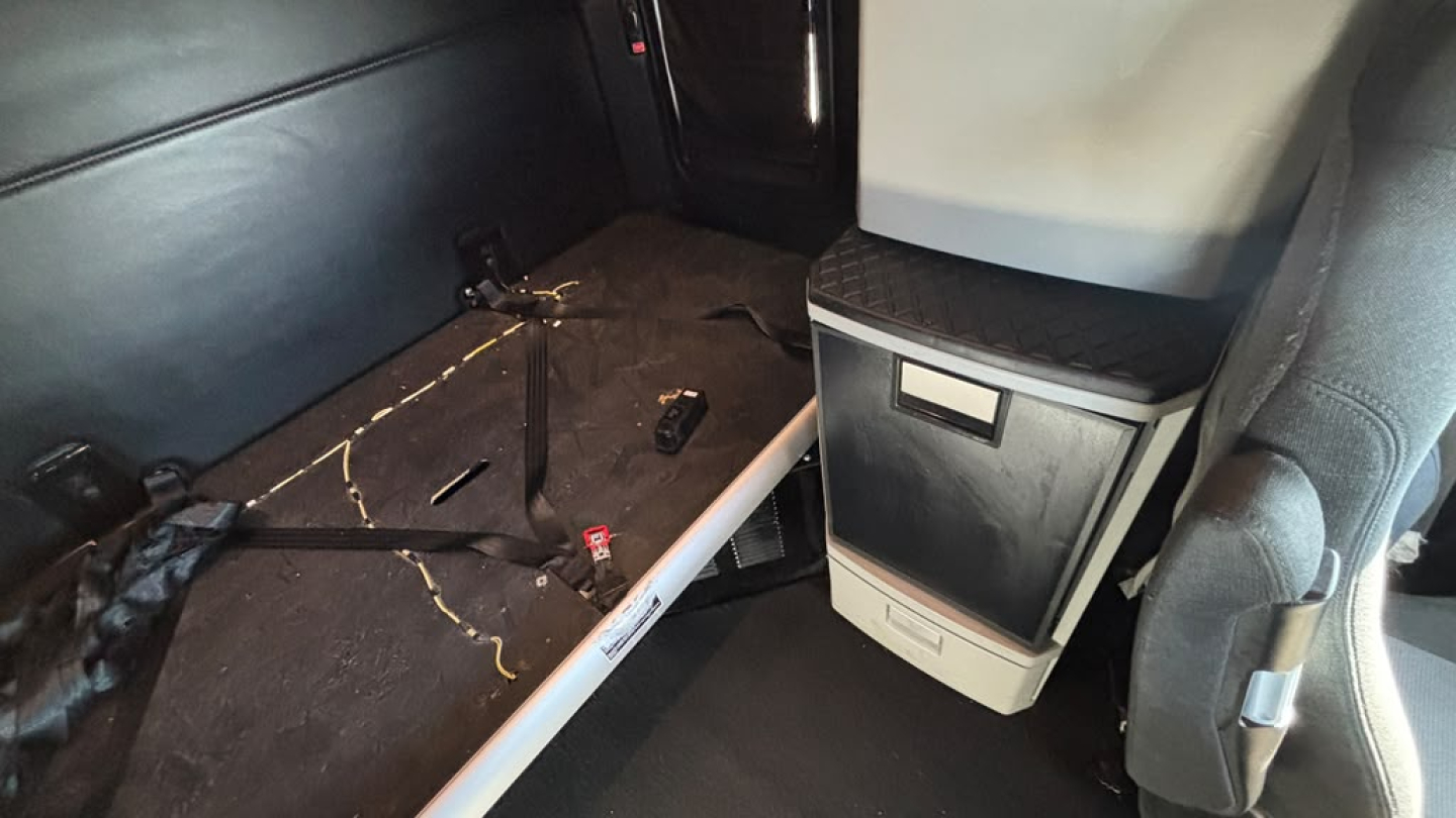 Kenworth T680 interior showing sleeper cab area with bench/step and storage cabinet; cables and seat rail visible.