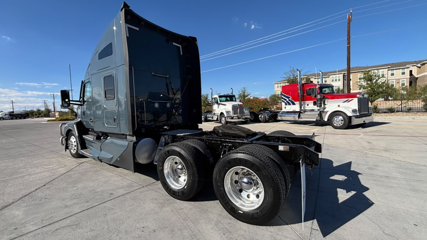 Kenworth T680 semi-truck in a dealership lot, side view showing cab and rear wheels, clear sky.