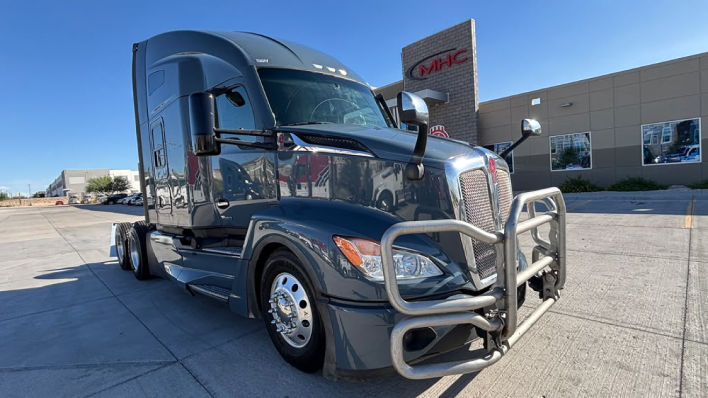 Kenworth T680 sleeper cab truck in a dealership lot with front bull bar and chrome accents.