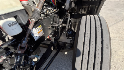 Kenworth T680 engine bay with front wheel and suspension components visible; various hoses and wires present.