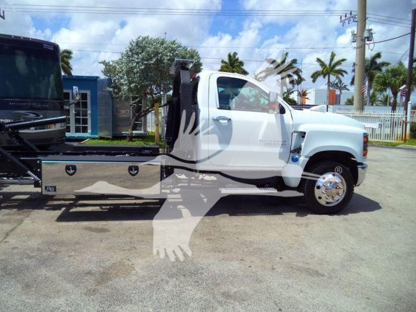 Truck chassis showing a white 2023 Chevrolet Silverado 6500HD rollback with a metal utility bed and side compartments.