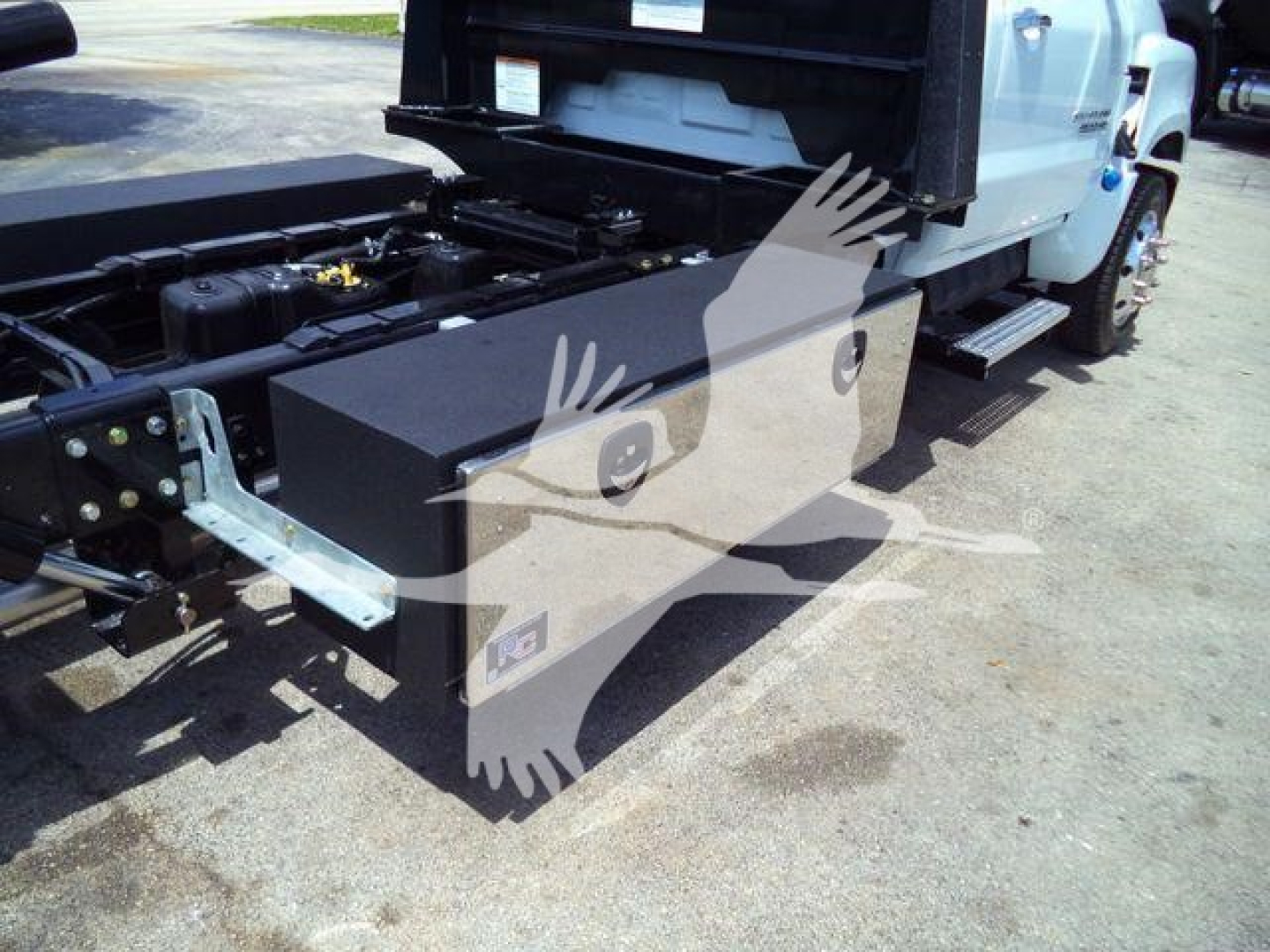 Truck bed toolbox and chassis area of a 2023 Chevrolet Silverado 6500HD rollback, showing a large rectangular black toolbox mounted on a dual rear setup with side steps.