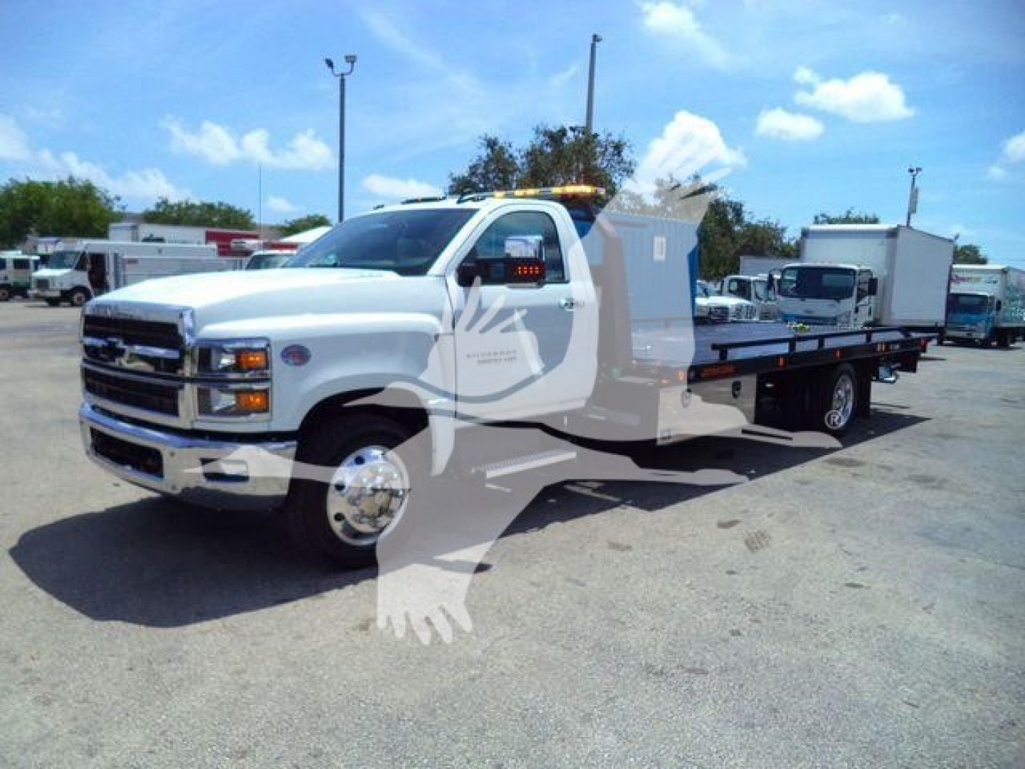 Truck in a rollback tow truck configuration showing a white Chevrolet Silverado 6500HD with flatbed, front grille, headlights, and side mirrors.