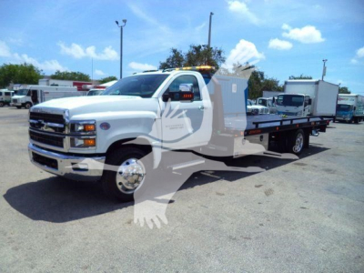 Truck in a rollback tow truck configuration showing a white Chevrolet Silverado 6500HD with flatbed, front grille, headlights, and side mirrors.