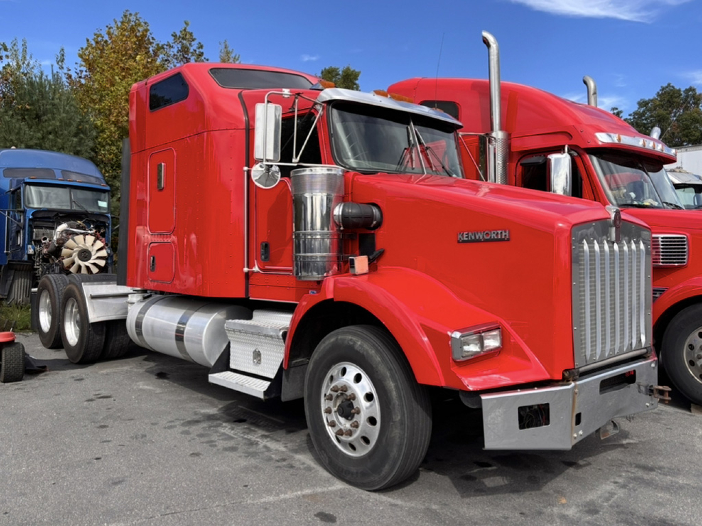 Kenworth T-800 truck with red sleeper cab and chrome grille, side exhaust stacks, parked among other trucks.