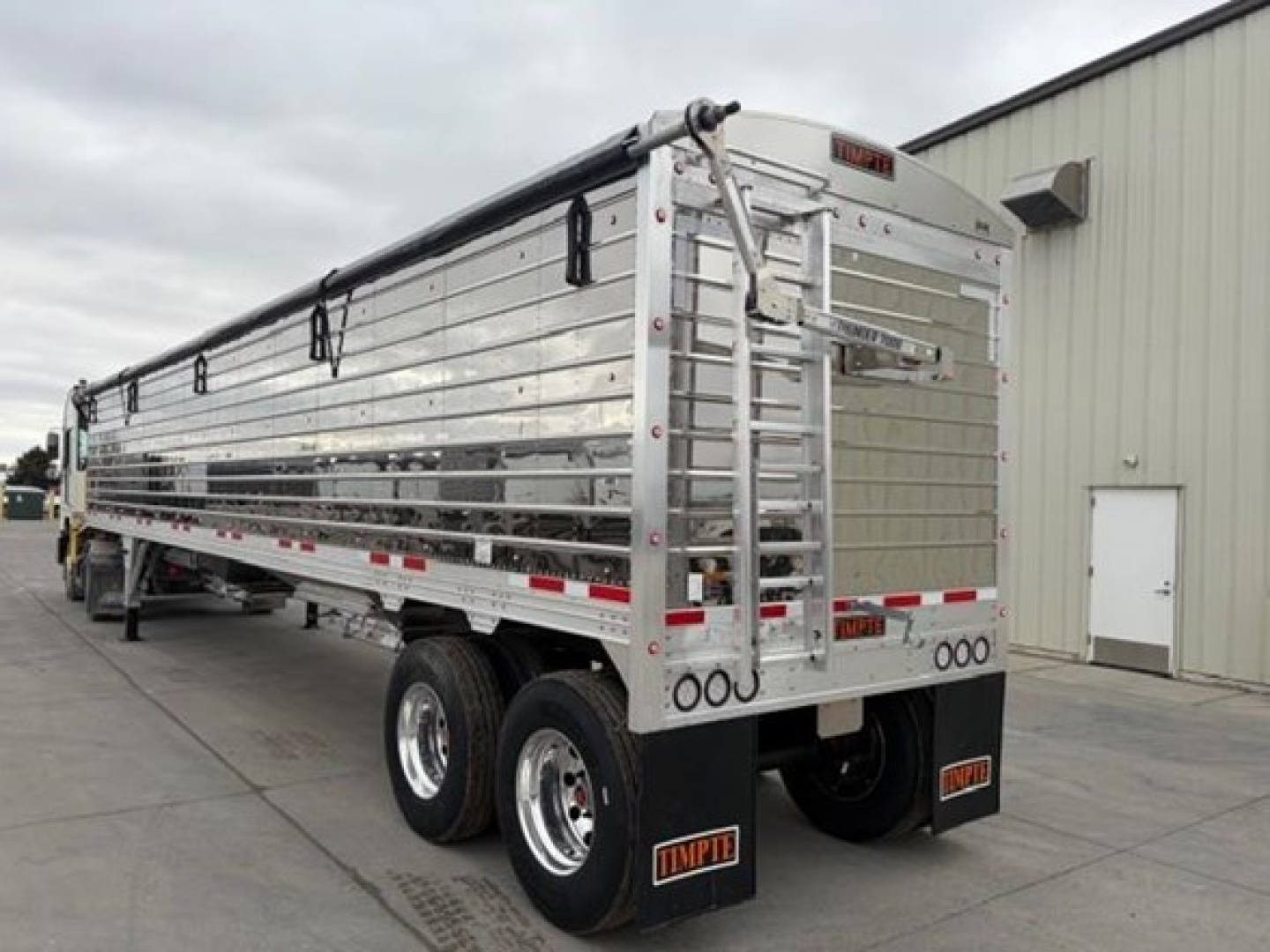Timpte Super Hopper trailer rear three-quarter view showing aluminum side panels, tandem axles, and rear gate with latching mechanism.