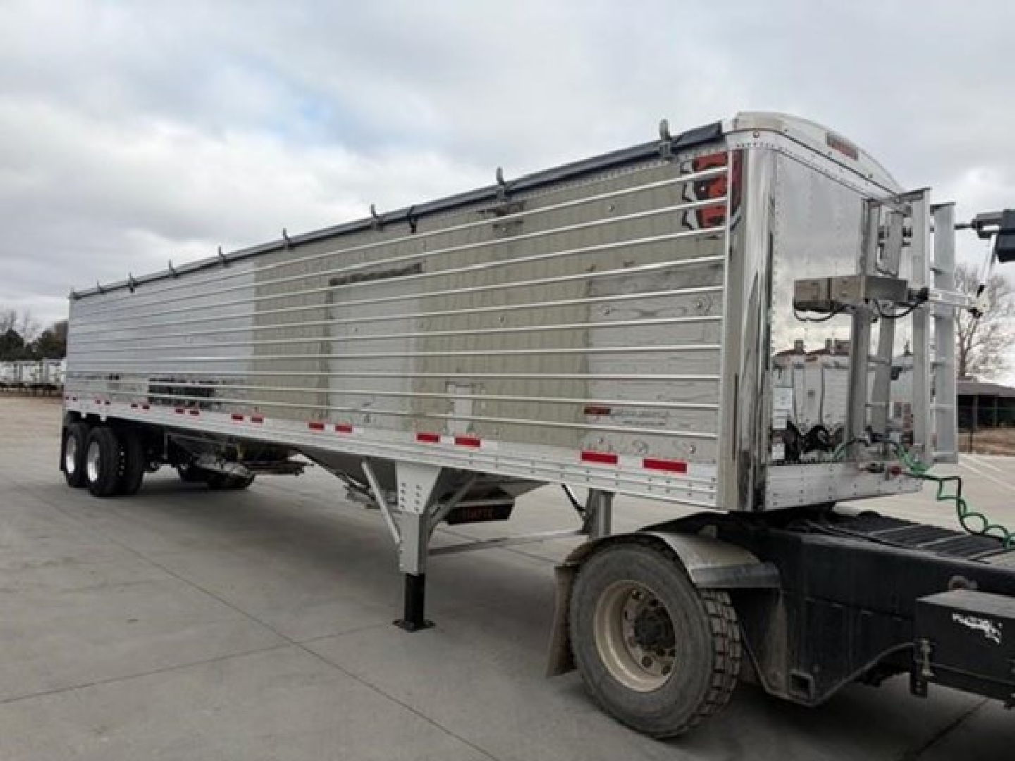 Trailer side view of a new 2026 Timpte Super Hopper grain trailer showing aluminum side panels and rear hopper mechanism.