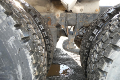 View under a 2005 International 9400 truck showing dual rear wheels, mud, and a leaf spring suspension with a visible differential and frame.