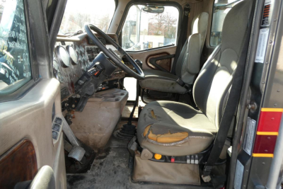 Interior of a 2005 International 9400 daycab showing worn driver and passenger seats, steering column, dashboard gauges, and manual gear shifter.