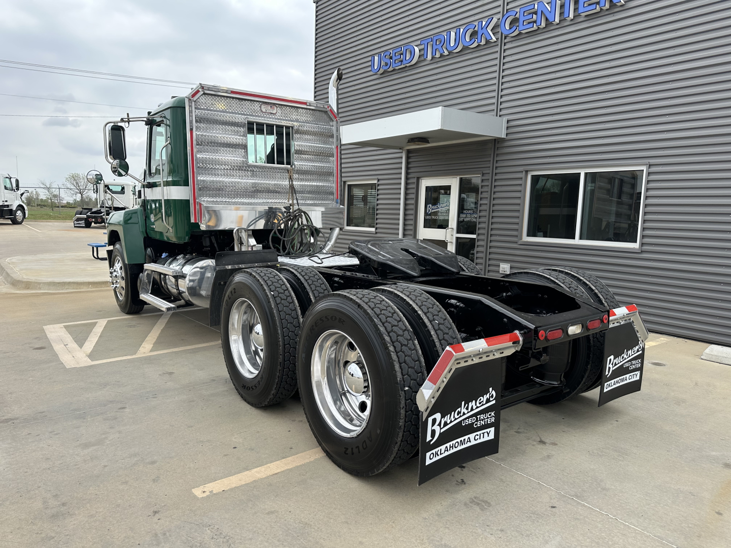 Mack PI64T daycab truck chassis rear view showing dual rear axles and semi-trailer connections in front of Used Truck Center building.